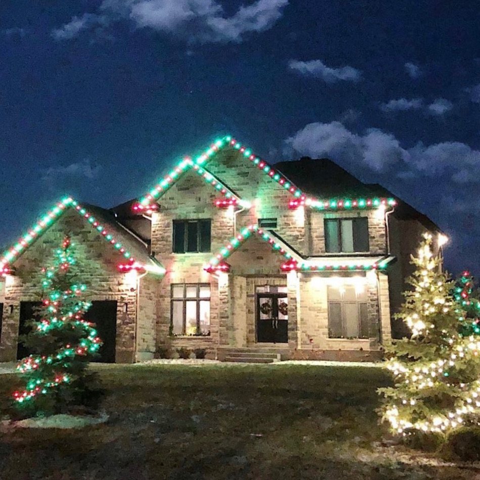 Large stone home with red and green roofline Christmas lights and matching wrapped trees